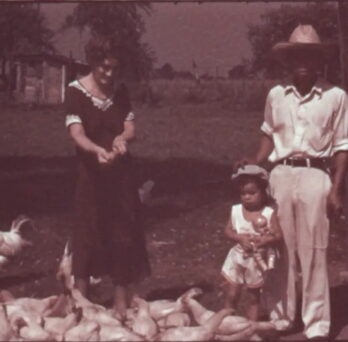 film still of a man, woman, and small child with chickens
                  